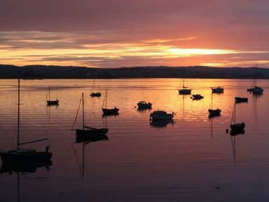 Several boats on calm water during sunset with hills in the background at 1 The Quay in Lympstone