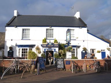 The exterior of The Swan Inn pub with bicycles parked outside and people near the entrance at 1 The Quay in Lympstone