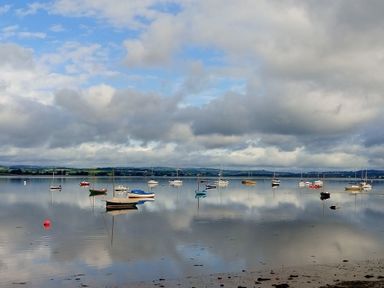 Boats anchored on calm water with cloudy sky and distant land at 1 The Quay in Lympstone
