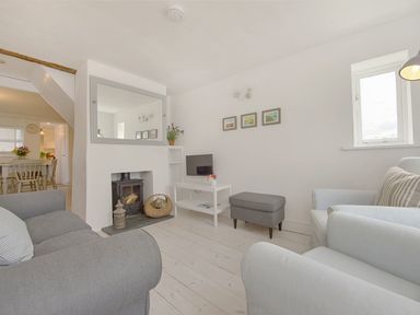 A living room with grey sofas a fireplace with a wood stove a white table with a small tv and a grey ottoman at 1 The Quay in Lympstone