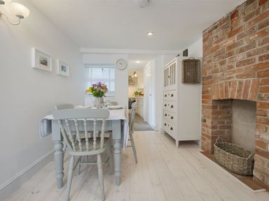 A dining area with a table and chairs a brick fireplace and a white cabinet at 1 The Quay in Lympstone