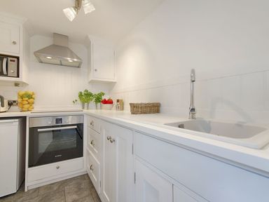 A kitchen with white cabinets a stainless steel oven and hood a sink and countertop with plants and fruit at 1 The Quay in Lympstone