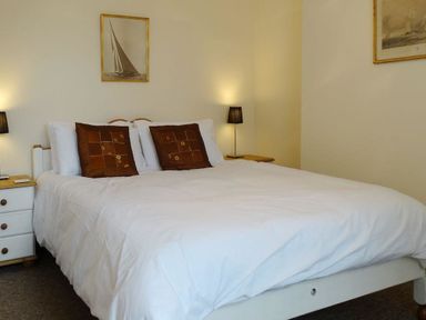 A bedroom with a double bed with white bedding and two brown pillows two bedside tables with lamps and framed pictures on the walls at 2 Carlton Mews in Exmouth