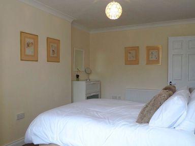 A bedroom with a white bed and pillows a white dresser with a mirror and framed pictures on the walls at 2 Carlton Mews in Exmouth