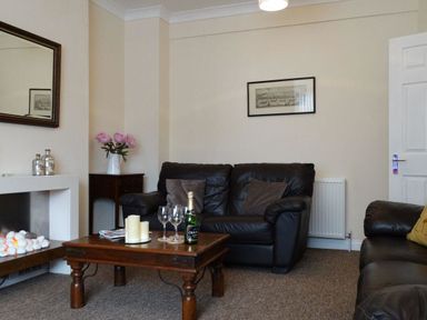 A living room with a leather sofa a wooden coffee table with glasses and candles and a fireplace at 2 Carlton Mews in Exmouth