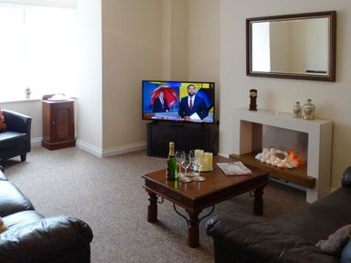 A living room with two leather sofas a wooden coffee table a fireplace and a television at 2 Carlton Mews in Exmouth