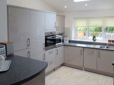 A kitchen with grey cabinets a built-in oven a microwave a sink and a window with plants on the sill at 2 Carlton Mews in Exmouth