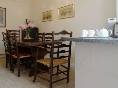 A wooden dining table with six chairs and a vase of flowers next to a kitchen counter with cups and a teapot at 2 Carlton Mews in Exmouth