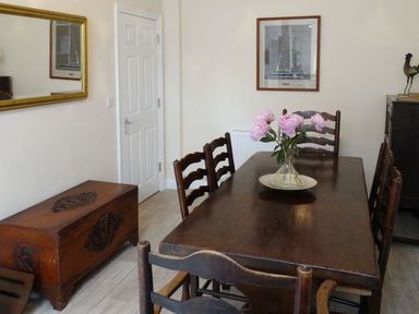A dining room with a wooden table and chairs a vase with flowers on the table a chest a mirror and a framed picture at 2 Carlton Mews in Exmouth