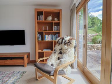 A living room with a chair and bookcase at The Old Log Shed in Honiton