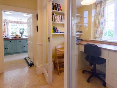 A hallway leading to a kitchen with blue cabinets and a small office with a desk and chair at Abbots Manor Combe Raleigh near Honiton