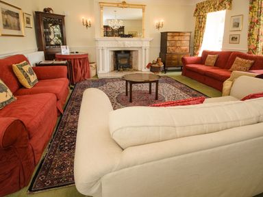 A living room with red and white sofas a round wooden table a fireplace and a large mirror at Abbots Manor in Combe Raleigh near Honiton