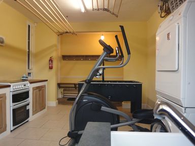 A utility room with an exercise bike a foosball table a cooker and a stacked washer and dryer at Abbots Manor Combe Raleigh near Honiton