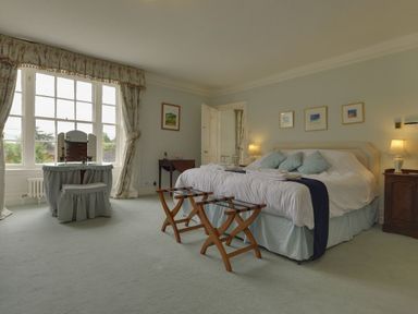 A bedroom with a large bed, bedside tables with lamps, a vanity table and chair near a window at Abbots Manor Combe Raleigh near Honiton