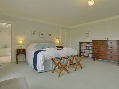 A bedroom with a large bed two wooden luggage racks a wooden chest of drawers and a bookshelf at Abbots Manor in Combe Raleigh near Honiton