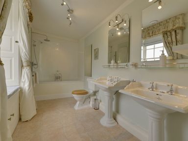 A bathroom with a bathtub shower toilet and two pedestal sinks at Abbots Manor Combe Raleigh near Honiton