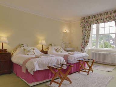 A bedroom with two single beds bedside tables lamps floral curtains and a window at Abbots Manor in Combe Raleigh near Honiton