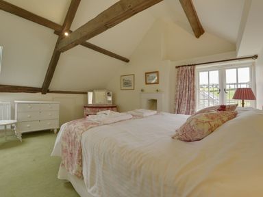 A bedroom with a double bed bedside table window and exposed wooden beams at Abbots Manor Combe Raleigh near Honiton