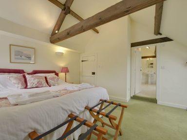 A bedroom with a double bed red pillows wooden luggage racks and an ensuite bathroom at Abbots Manor Combe Raleigh near Honiton