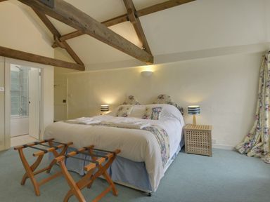 A bedroom with a double bed bedside tables lamps wooden luggage racks and exposed wooden beams at Abbots Manor in Combe Raleigh near Honiton