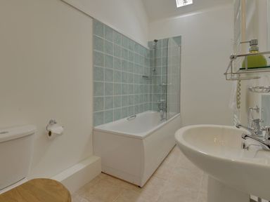 A bathroom with a toilet with a wooden seat a bathtub with blue tiles and a shower and a white sink at Abbots Manor in Combe Raleigh near Honiton