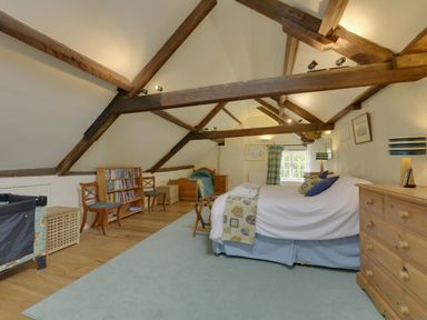 A bedroom with exposed wooden beams a large bed two chairs a bookshelf and a window at Abbots Manor in Combe Raleigh near Honiton
