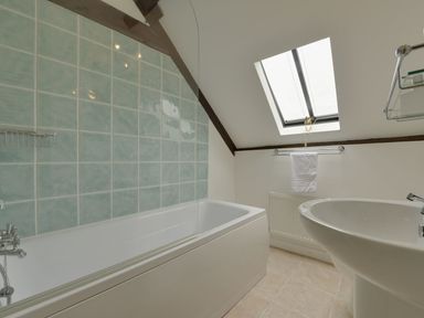 A bathroom with a bathtub, tiled wall, a skylight window, towel rack with a towel, and a pedestal sink at Abbots Manor in Combe Raleigh near Honiton