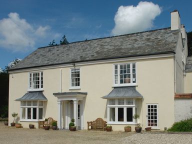 A cream colored house with white framed windows and benches outside at Abbots Manor in Combe Raleigh near Honiton