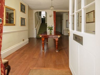 A hallway with wooden floor a wooden table with a flower vase and a staircase at Abbots Manor in Combe Raleigh near Honiton