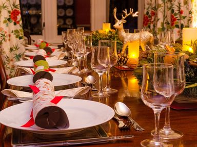 A dining table set with plates wine glasses cutlery and Christmas crackers with a decorative reindeer and candles at Abbots Manor in Combe Raleigh near Honiton