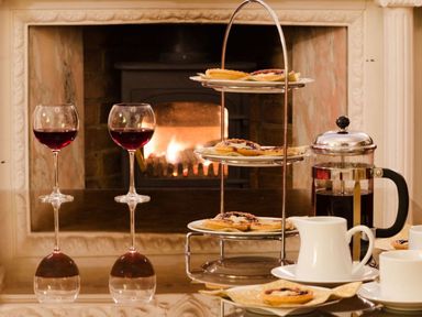 A dining table with two glasses of red wine a tiered tray of pastries a coffee press and cups in front of a fireplace at Abbots Manor in Combe Raleigh near Honiton