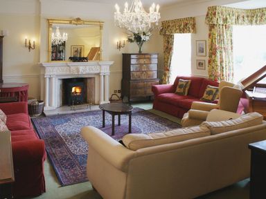 A living room with sofas armchairs floral curtains a fireplace and a chandelier at Abbots Manor in Combe Raleigh near Honiton