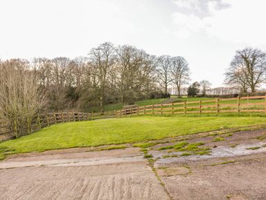 A grassy yard with a wooden fence and trees in the background at The Old Stable in Sidbury near Sidmouth