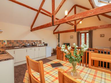 An open plan kitchen and dining area with wooden beams and a table with flowers at The Old Stable in Sidbury near Sidmouth