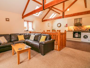 An open living room and kitchen with a brown leather sofa wooden coffee table wooden beams and dining table at The Old Stable in Sidbury near Sidmouth