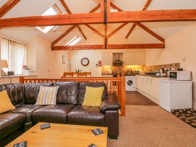 An open plan living area with a leather sofa and cushions a wooden dining table and a kitchen with white cabinets at The Old Stable in Sidbury near Sidmouth