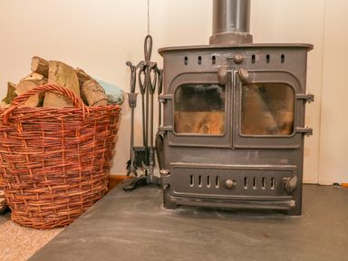 A wood burning stove with fireplace tools and a basket of firewood at The Old Stable in Sidbury near Sidmouth