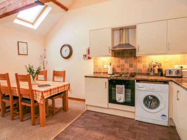 A kitchen and dining area with a wooden table and chairs and kitchen appliances at The Old Stable in Sidbury near Sidmouth