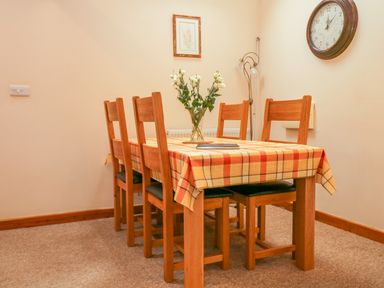 A dining room with a wooden table covered with a checkered tablecloth and six chairs at The Old Stable in Sidbury near Sidmouth