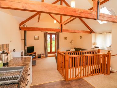 An open plan living room and kitchen with wooden beams and staircase at The Old Stable in Sidbury near Sidmouth