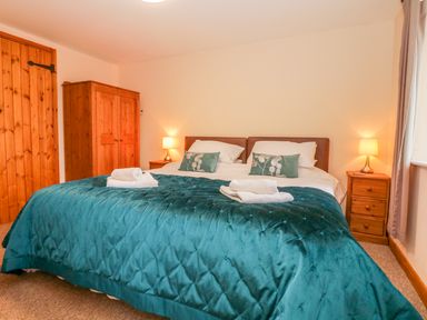 A bedroom with a double bed two bedside tables with lamps a wooden wardrobe and door at The Old Stable in Sidbury near Sidmouth