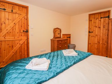 A bedroom with a bed covered in a teal quilt and white towels on top two wooden doors and a wooden dresser with a mirror at The Old Stable in Sidbury near Sidmouth
