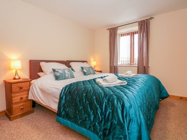 A bedroom with a double bed with teal bedding and pillows beside wooden nightstands with lamps at The Old Stable in Sidbury near Sidmouth