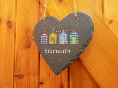 A heart-shaped slate hanging on a wooden door with illustrations of colorful beach huts and the word Sidmouth at The Old Stable in Sidbury near Sidmouth