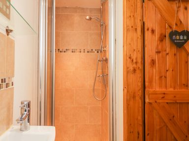 A shower area with tiled walls a handheld shower head a sink with a faucet and a wooden door with a hanging ornament at The Old Stable in Sidbury near Sidmouth