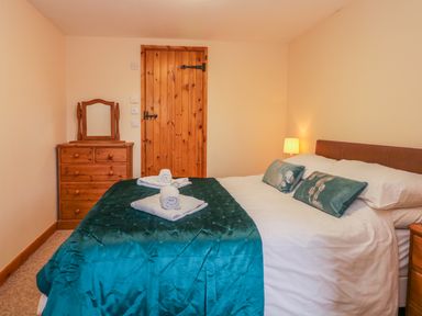 A bedroom with a double bed with teal bedding and pillows wooden dresser with mirror and wooden door at The Old Stable in Sidbury near Sidmouth