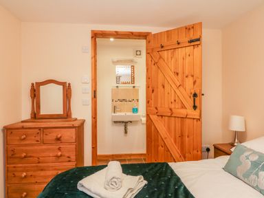 A bedroom with a wooden dresser and mirror a bed with folded towels an open wooden door revealing a bathroom sink at The Old Stable in Sidbury near Sidmouth