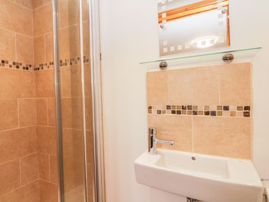 A bathroom with a tiled shower area and a white sink with a faucet at The Old Stable in Sidbury near Sidmouth