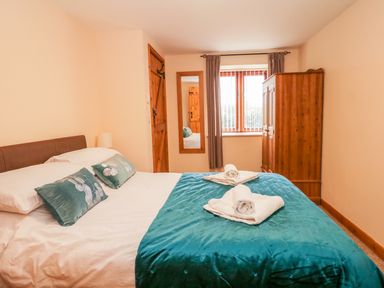 A bedroom with a double bed with teal bedding and pillows a wooden wardrobe and a wall mirror at The Old Stable in Sidbury near Sidmouth
