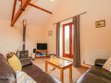 A living room with two brown leather sofas a wood stove a wooden coffee table and double doors with curtains at The Old Stable in Sidbury near Sidmouth